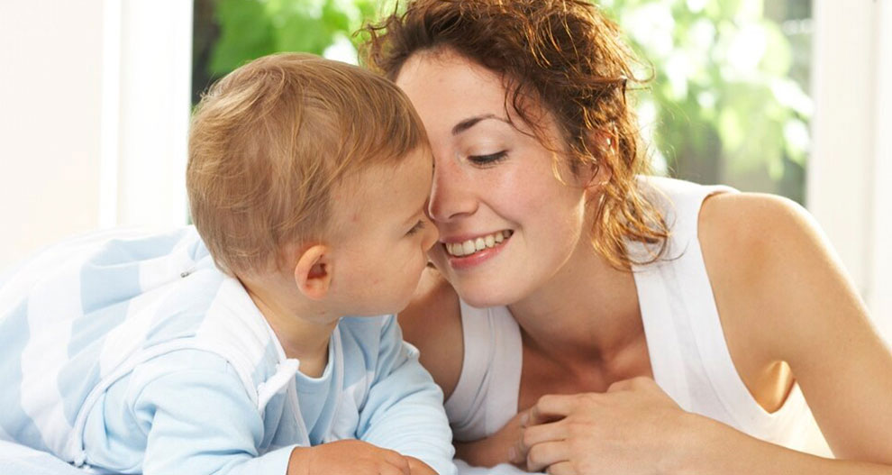 Une femme et un bébé sont allongés sur un lit, la femme regardant affectueusement le bébé.