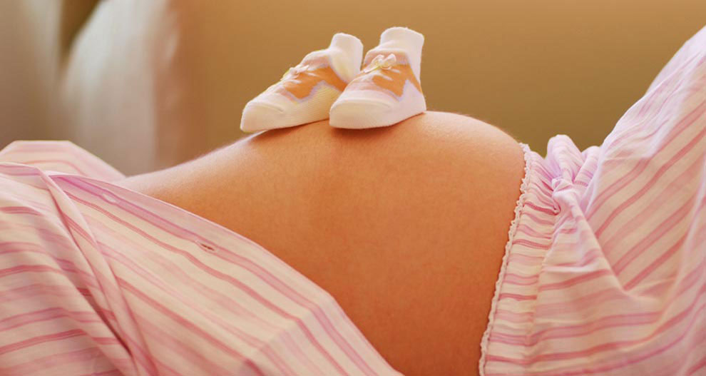 Le ventre d'une femme enceinte est orné d'une paire de chaussures pour bébé.