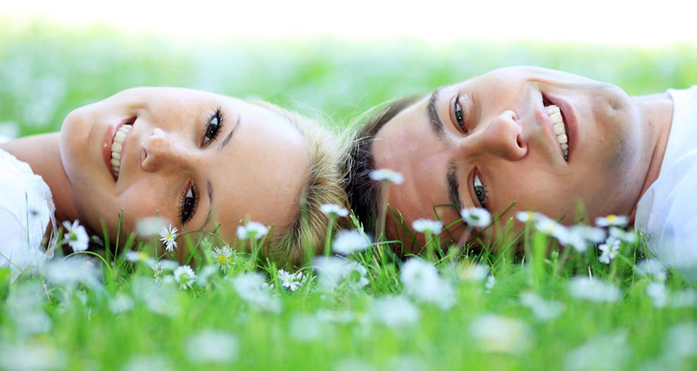 Deux personnes sont allongées sur de l'herbe entourée de fleurs et regardent vers la caméra.