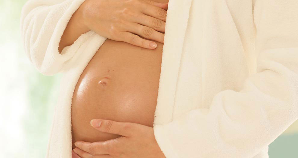 Une femme enceinte, vêtue d'une robe blanche, berce doucement son ventre.
