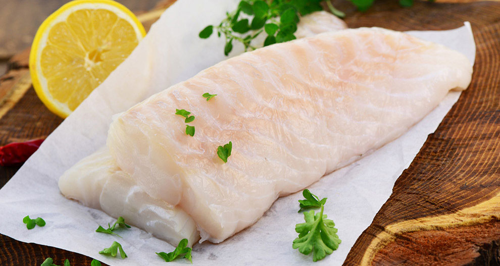Un filet de poisson cru est présenté sur une planche en bois, accompagné d'un quartier de citron et de persil frais.