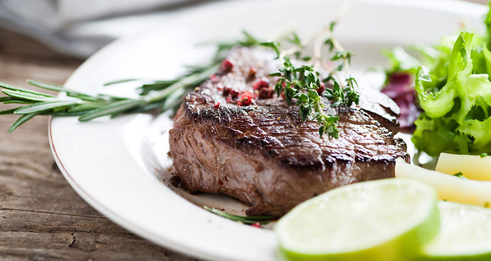 Un steak garni de romarin et de thym, accompagné d'une salade verte et de tranches de citron vert.