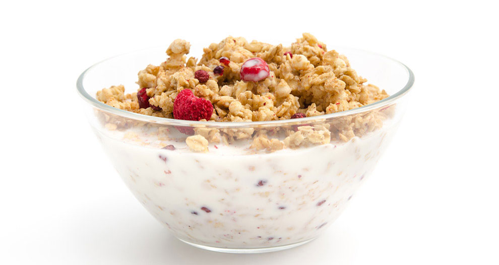 Un bol transparent rempli de granola et de baies rouges, partiellement immergé dans un liquide blanc.