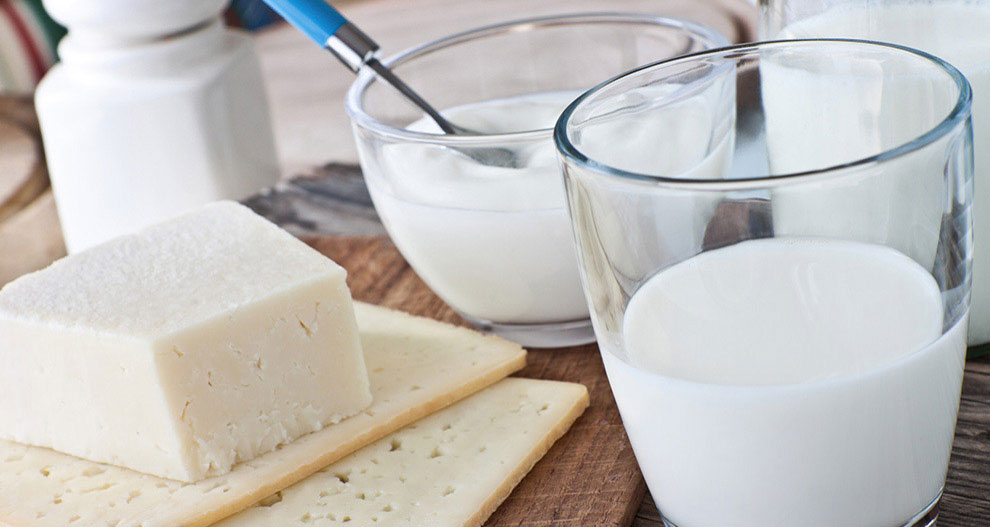 Un verre de lait, un bol de yaourt, du fromage et des crackers sur une table en bois.
