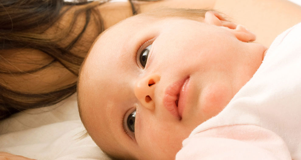 Gros plan sur le visage d'un bébé, partiellement caché par les cheveux d'une personne.