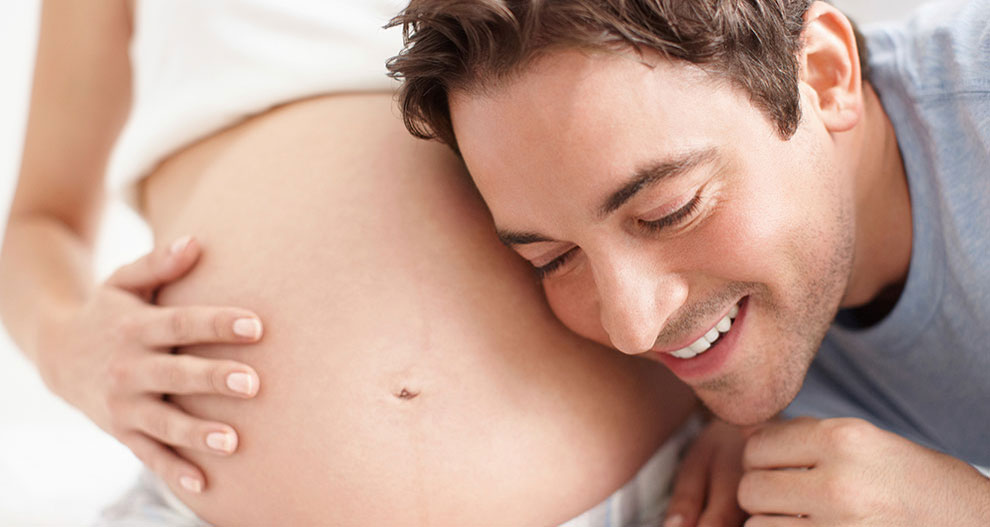 Un homme enlace le ventre d'une femme enceinte.