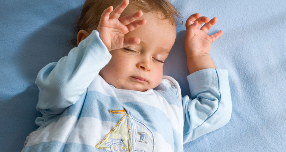 Un bébé est allongé sur une surface bleue, vêtu d'un ensemble bleu clair avec un motif de voilier.