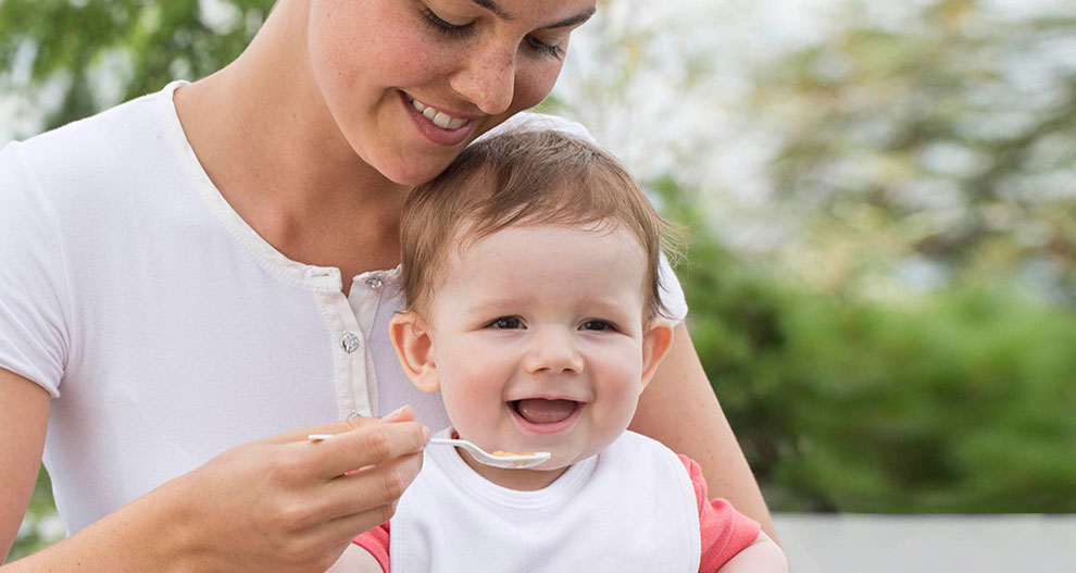 Une femme en chemise blanche nourrit un bébé avec une cuillère.