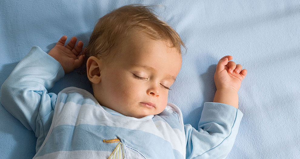 Un bébé est allongé sur une surface bleue, vêtu d'un ensemble rayé bleu clair et blanc avec un motif de voilier.
