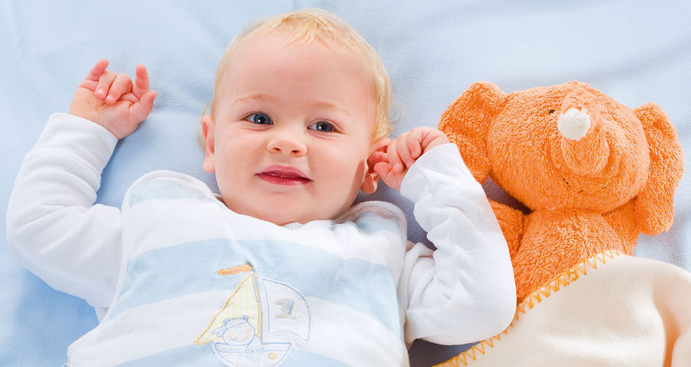 Un bébé est allongé sur une couverture bleue et tient un éléphant en peluche.