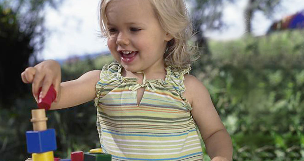 Un jeune enfant joue avec des blocs colorés à l'extérieur.