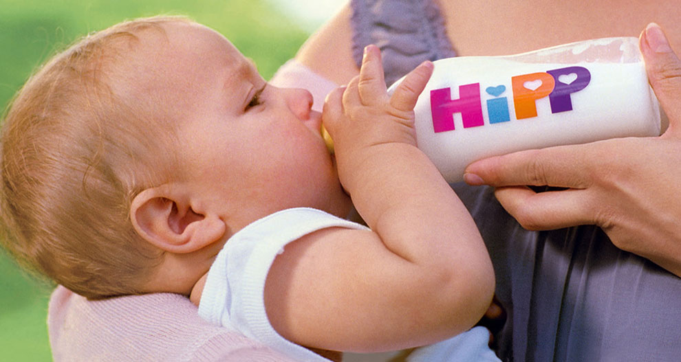 Un bébé boit dans un biberon portant le mot "HiPP".