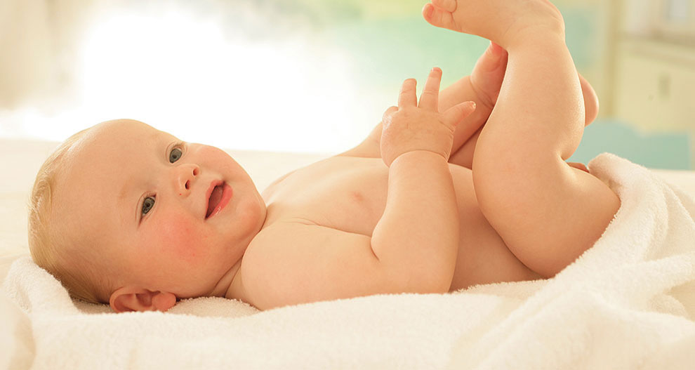 Un bébé est allongé sur une serviette blanche et regarde vers le haut en levant la main.
