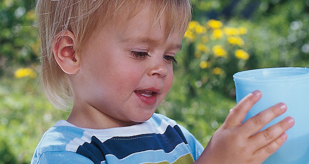 Un jeune enfant tient un gobelet bleu à l'extérieur.