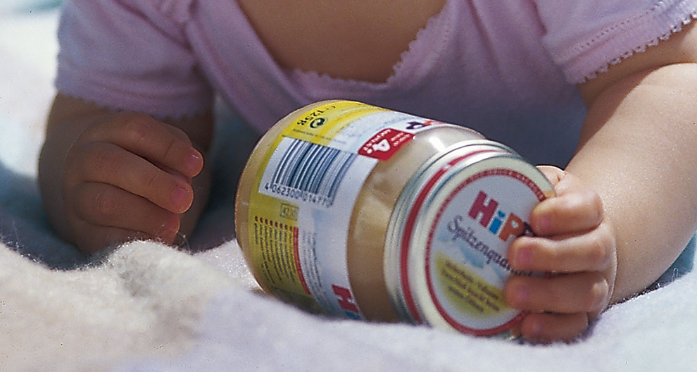 La main d'un bébé saisit un pot avec un code-barres et une étiquette.