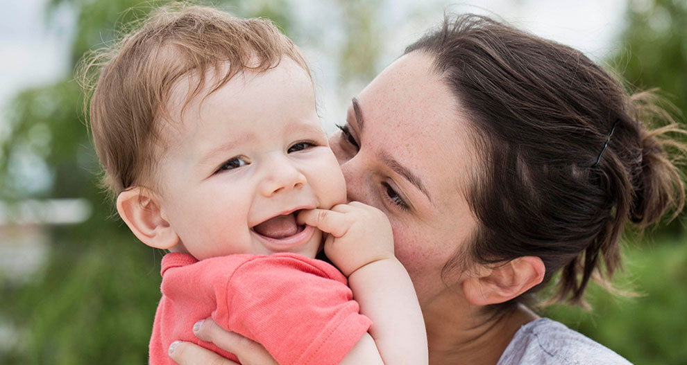 Une femme tient affectueusement un bébé rieur en plein air.