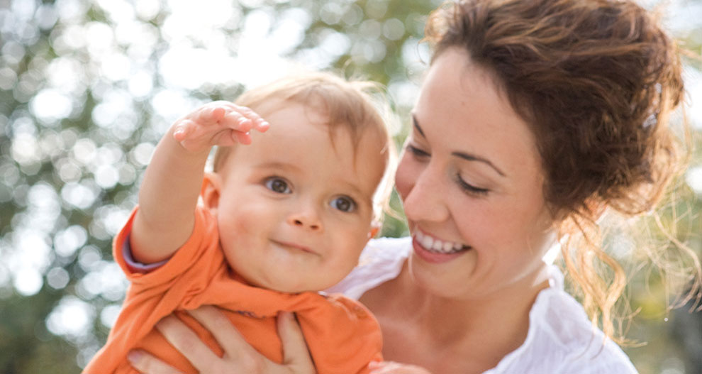 Une femme tient un bébé à l'extérieur.