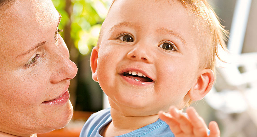 Gros plan d'une femme et d'un bébé, la femme regardant vers le bas le bébé, qui regarde vers le haut avec un sourire.