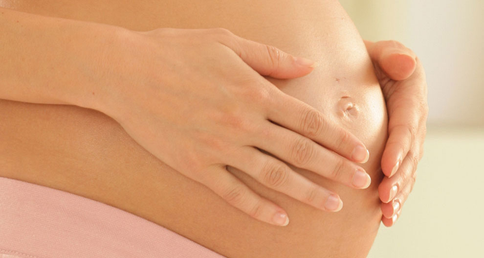 Les mains d'une femme enceinte se posent délicatement sur son ventre.