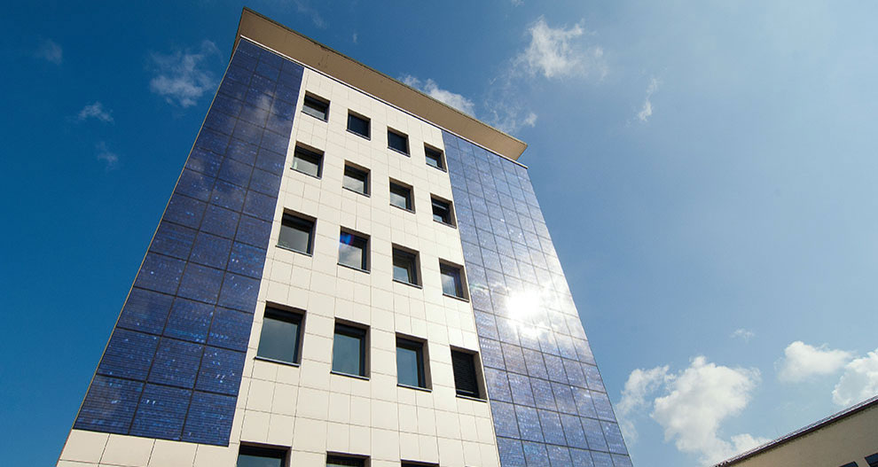 Un bâtiment moderne à la façade blanche et bleue se dresse sous un ciel clair avec quelques nuages.
