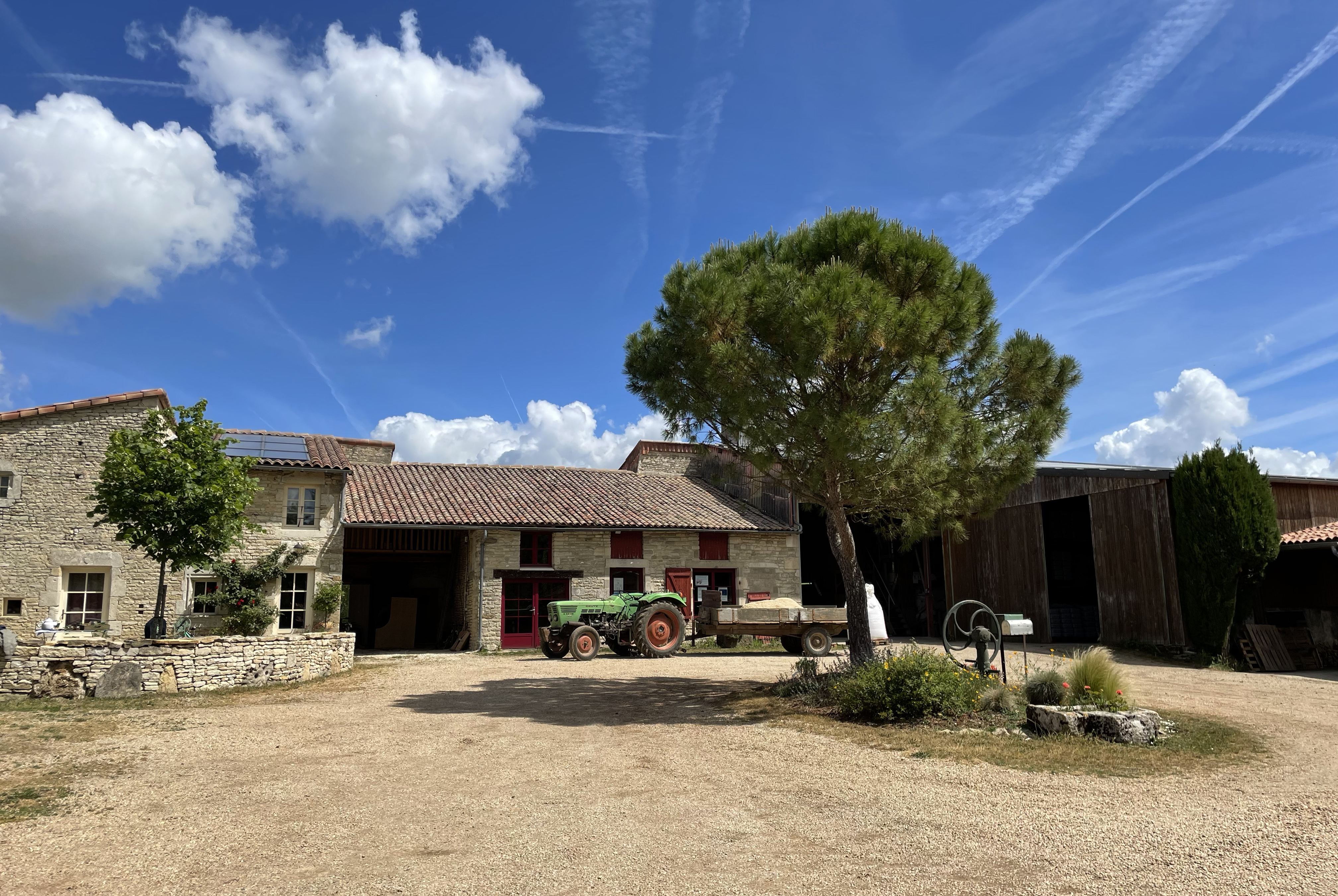 Un bâtiment en pierre avec un toit rouge, un tracteur vert et un ciel bleu avec des nuages blancs.