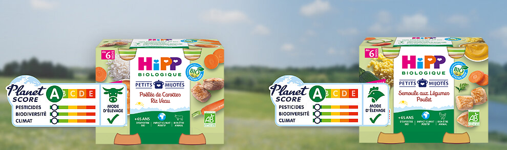 Deux boîtes d'aliments pour bébés Hipp portant l'étiquette Planet Score, l'une avec une carotte et l'autre avec une légumineuse, sont présentées sur un fond naturel flou.