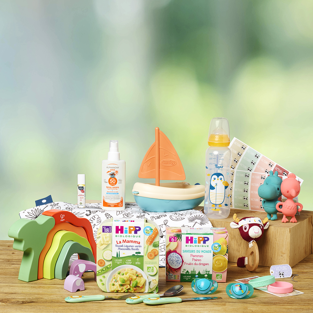 Une collection de produits et de jouets pour bébés, dont un biberon, un voilier, un arc-en-ciel en bois, une boîte de nourriture et un spray solaire.