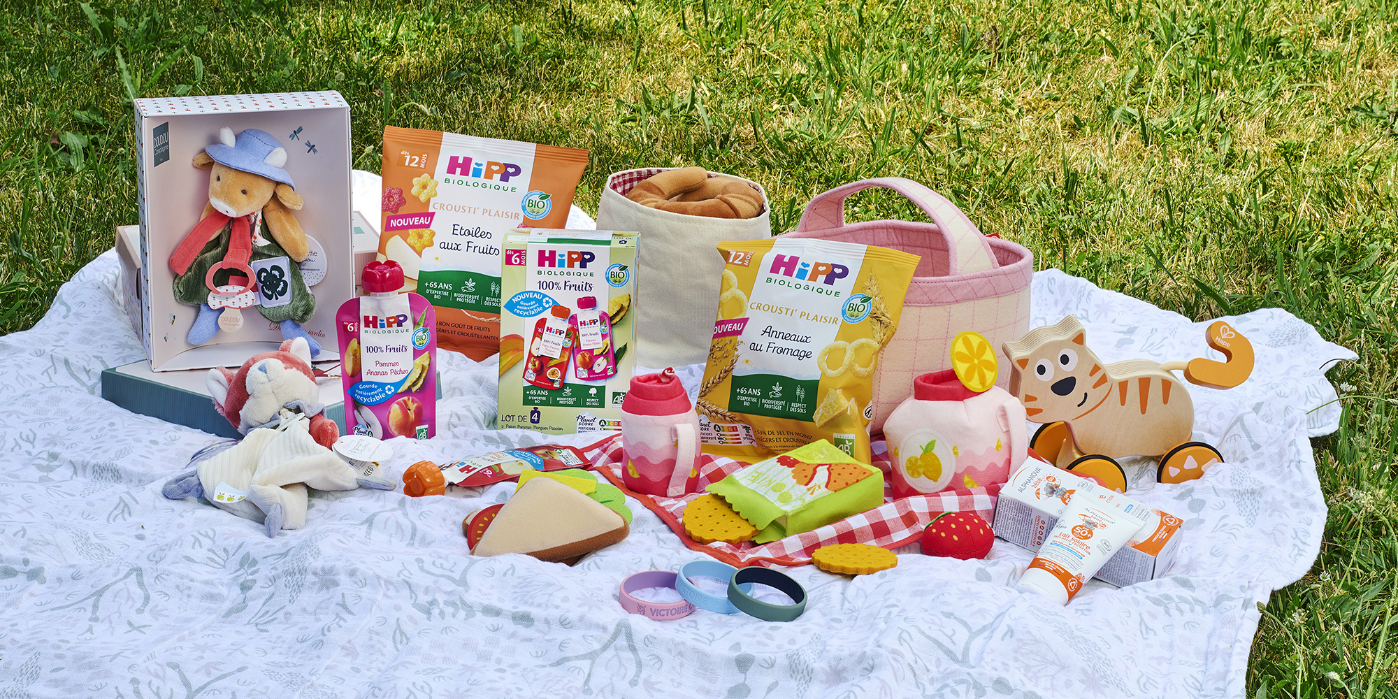 Scène de pique-nique avec une variété de produits et de jouets pour enfants étalés sur une couverture.