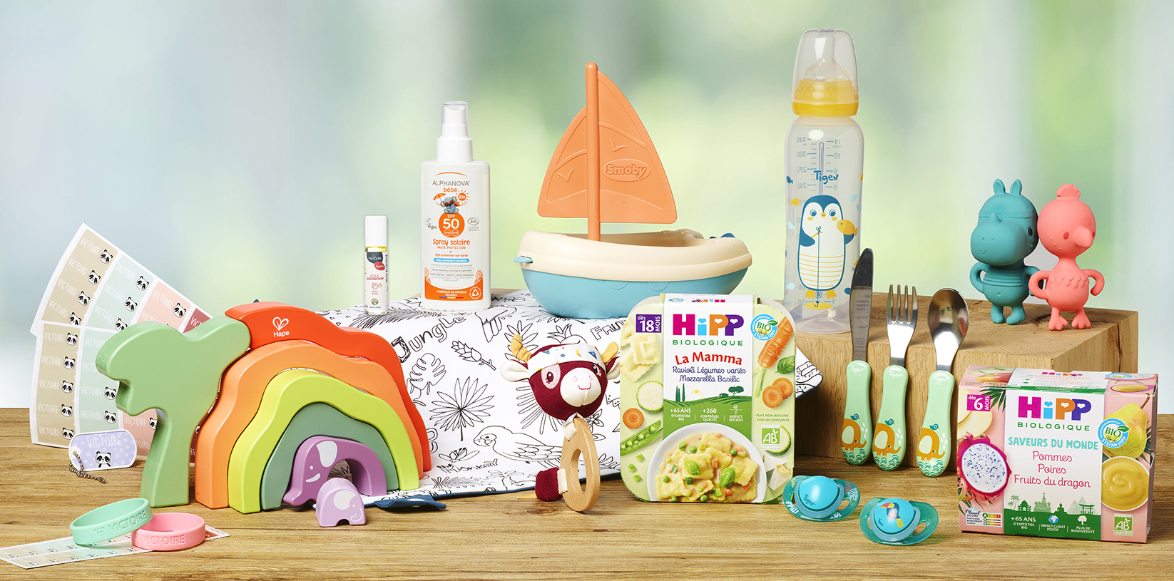 Une collection de produits et de jouets pour bébés, dont un biberon, un voilier, un jouet à empiler coloré, une tétine et une boîte d'aliments biologiques pour bébés.