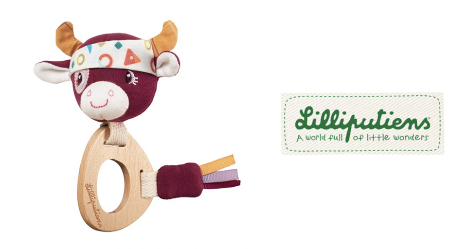 Une vache en peluche avec un bandana et une longe en bois attachée à sa queue est présentée à côté d'un logo vert et blanc avec le texte "Lilliputiens - Un monde plein de petites merveilles".