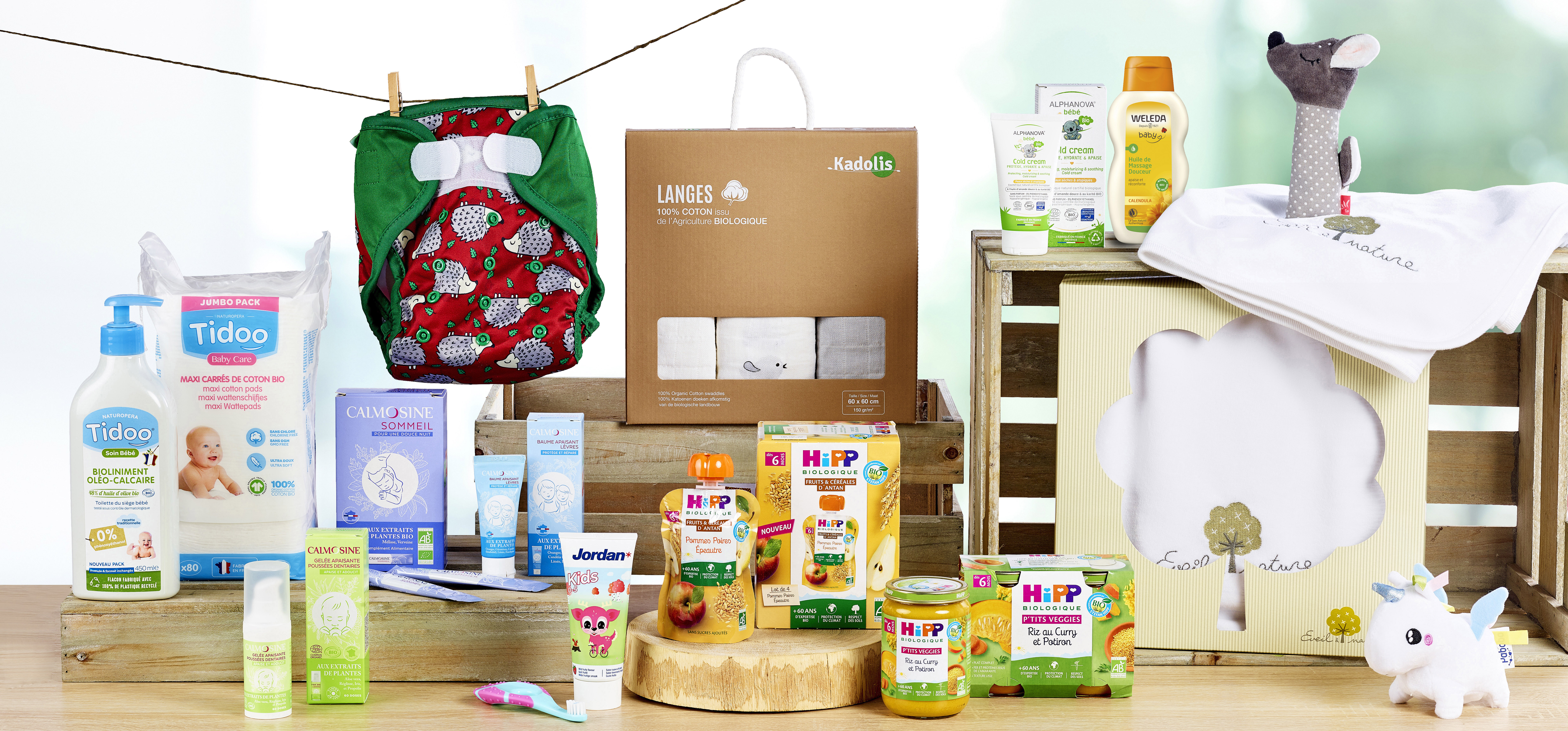 Divers produits et accessoires pour bébés, dont une couche, des lingettes, des crèmes et des aliments, disposés sur une surface en bois.