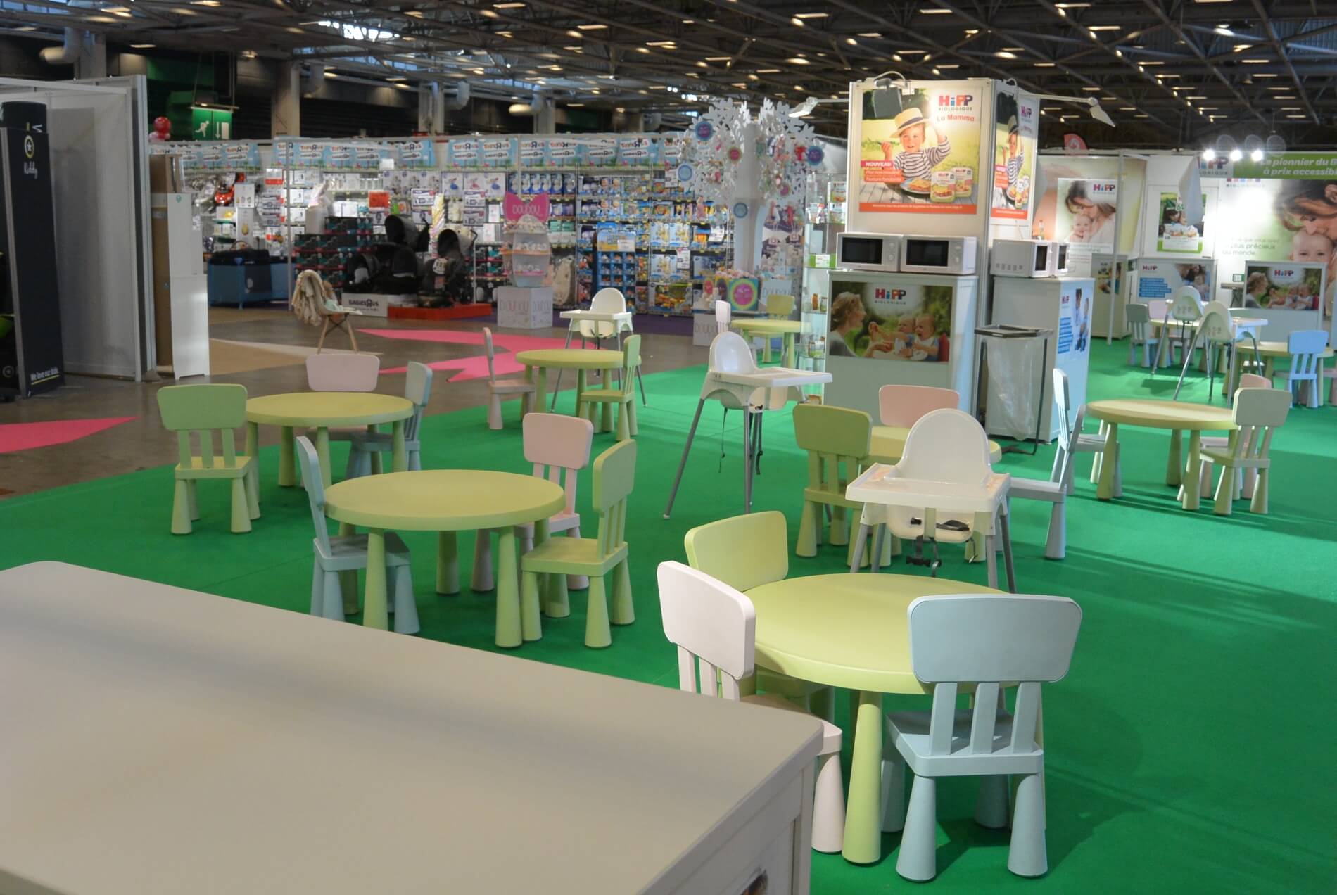 Une opportunité de jouer pour les petits Un cadre intérieur avec une variété de meubles et de produits pour enfants, y compris des tables, des chaises et des chaises hautes, présentés sur un sol recouvert d'une moquette verte.